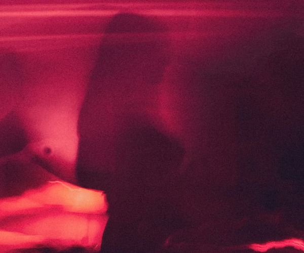 Silhouette of a person meditating against a soft pink background.